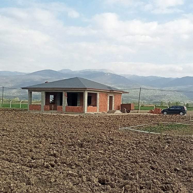 Sürülmüş tarlanın ortasındaki bahçe evi ve arkadaki dağlar