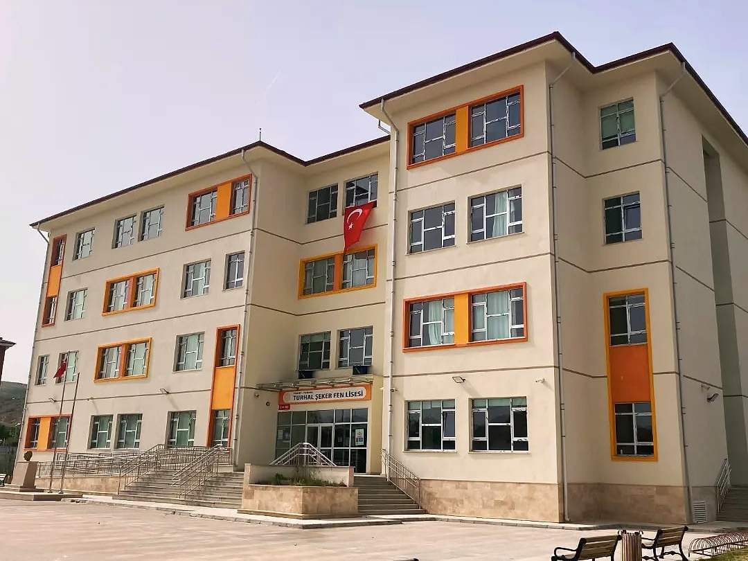 Şeker Fen Lisesi binasının krem ve turuncu cepheli ön görünümü, önünde banklar